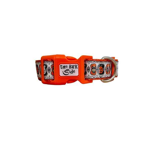 Dog collar featuring a spooky Halloween themed design on a white ribbon. The collar has orange webbing and buckle.