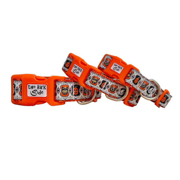 Three different sized dog collars featuring a spooky Halloween themed design on a white ribbon. The collars have orange webbing and buckles.