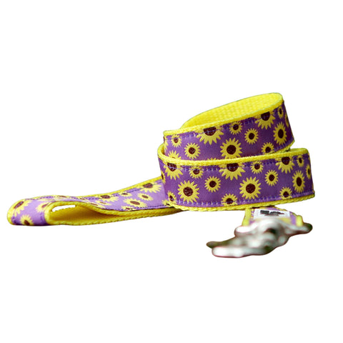 Close up of a dog leash with a cheerful sunflower design. The leash features a purple ribbon with pattern of bright yellow sunflowers on yellow webbing.